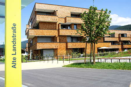 Wohnhäuser in der alten Landstraße in Röthis mit einer Bushaltestelle im Vordergrund.